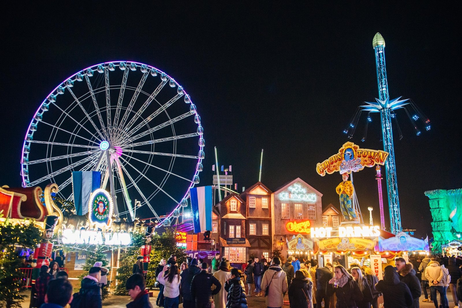 Grande roue illuminée, enseigne Santa Land et chalets de Hyde Park Winter Wonderland la nuit, avec la foule dans les allées