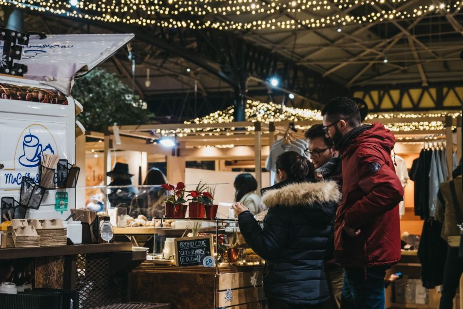 Shoppers at a stall with poinsettias under strings of fairy lights inside Old Spitalfields Market