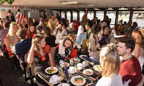 Convives au déjeuner de Noël dans le salon chauffé d’un bateau sur la Tamise