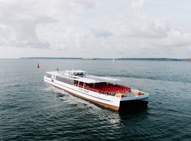 The Silver Raven, a white electric boat with an open deck of red seats, sailing by day
